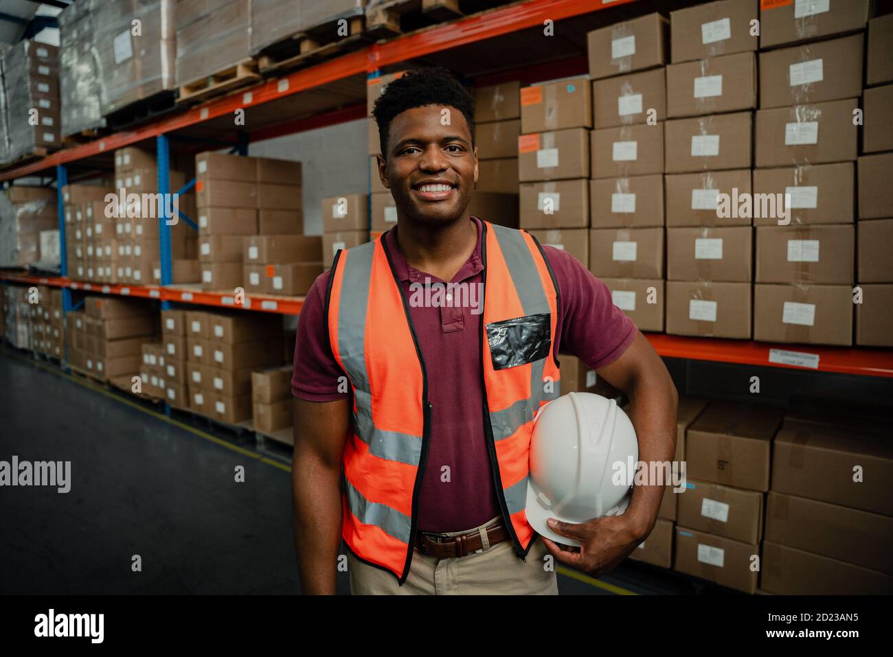 Bel maschio che tiene il hardhat che lavora in fabbrica negozio imballaggio pacchi per la consegna Foto Stock