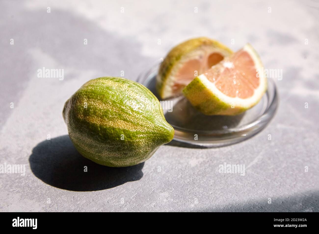 Limone rosa o limone Eureka variegato in piatto di vetro su tavola di cemento. Agrumi con scorza striata. Limone tagliato a metà con polpa rosa Foto Stock