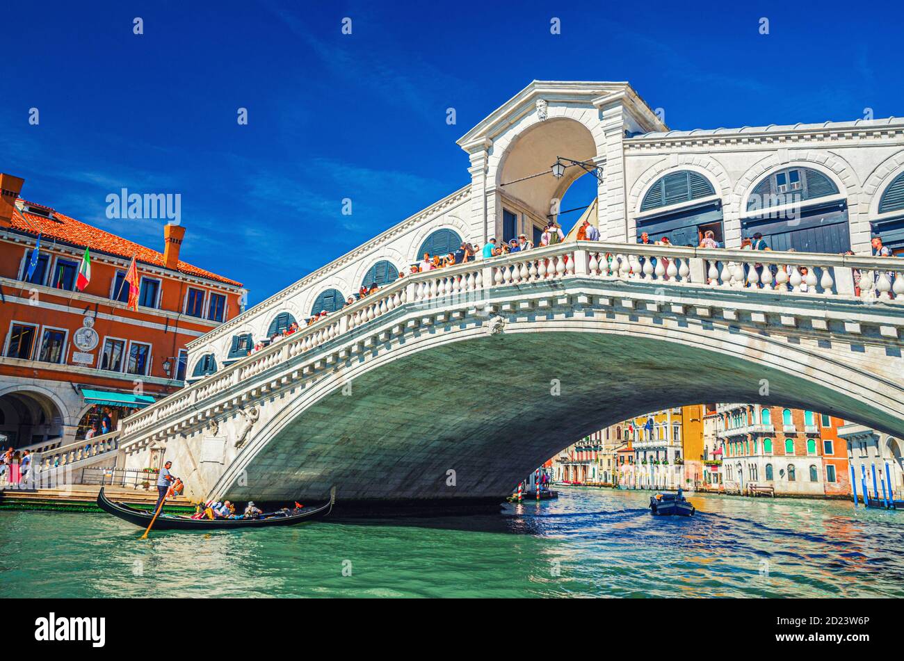 Venezia, Italia, 13 settembre 2019: Gondoliere in gondola tradizionale barca a vela sulle acque del Canal Grande sotto il Ponte di Rialto, tipici edifici colorati e cielo blu chiaro sfondo Foto Stock