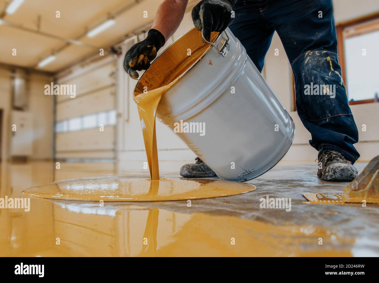 Operatore che applica un secchio di resina epossidica giallo sul pavimento. Foto Stock