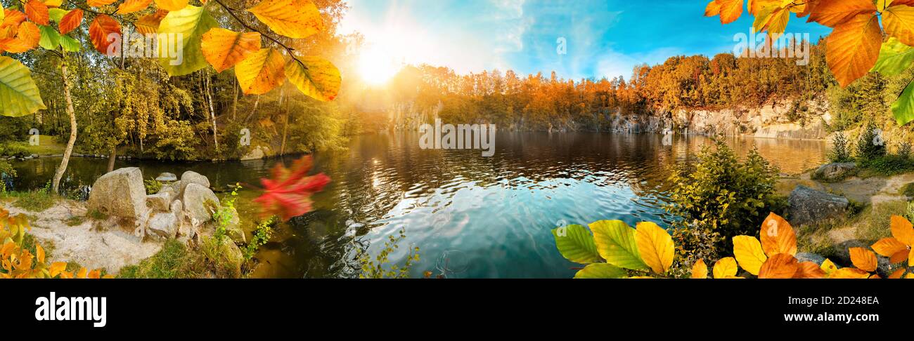 Magnifico panorama paesaggistico autunnale con fogliame colorato che incornicia un bellissimo lago blu, con sole e cielo blu Foto Stock