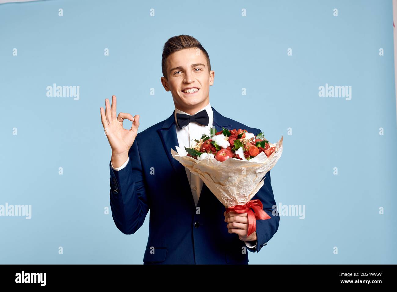 uomo romantico con bouquet di fiori e in un fascetta ad arco su sfondo blu vista ritagliata Foto Stock