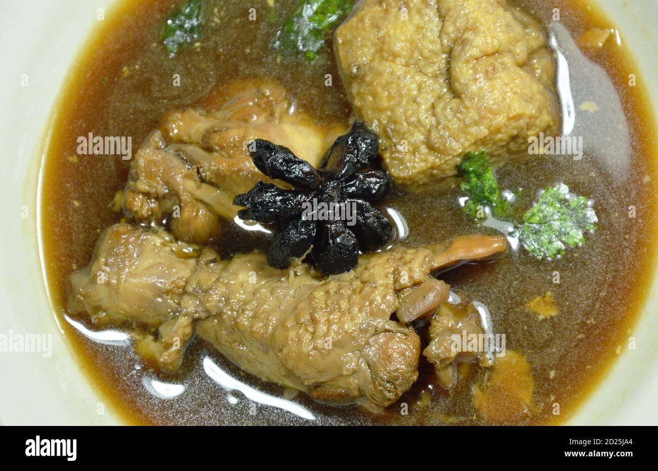 Coscia di pollo bollita e tofu fritto con erbe cinesi in zuppa marrone sul recipiente Foto Stock