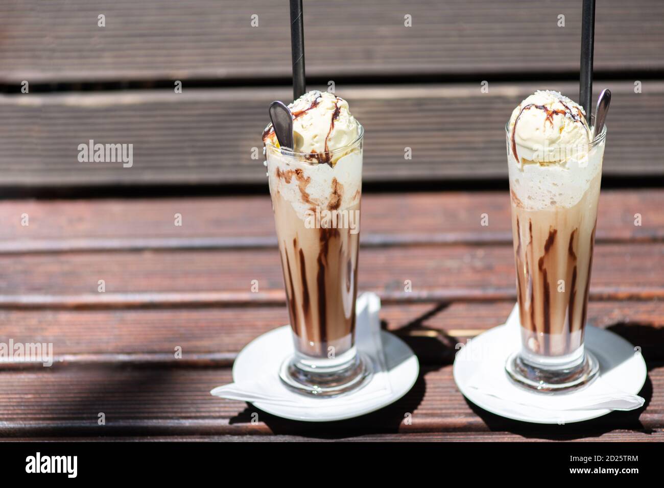 Il caffè ghiacciato su un tavolo di legno con il panna che viene versato in esso mostrando la consistenza e l'aspetto rinfrescante della bevanda. Foto Stock