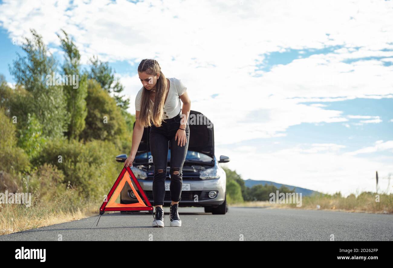 Ragazza che mette guasto segnalazione triangolo auto Foto Stock
