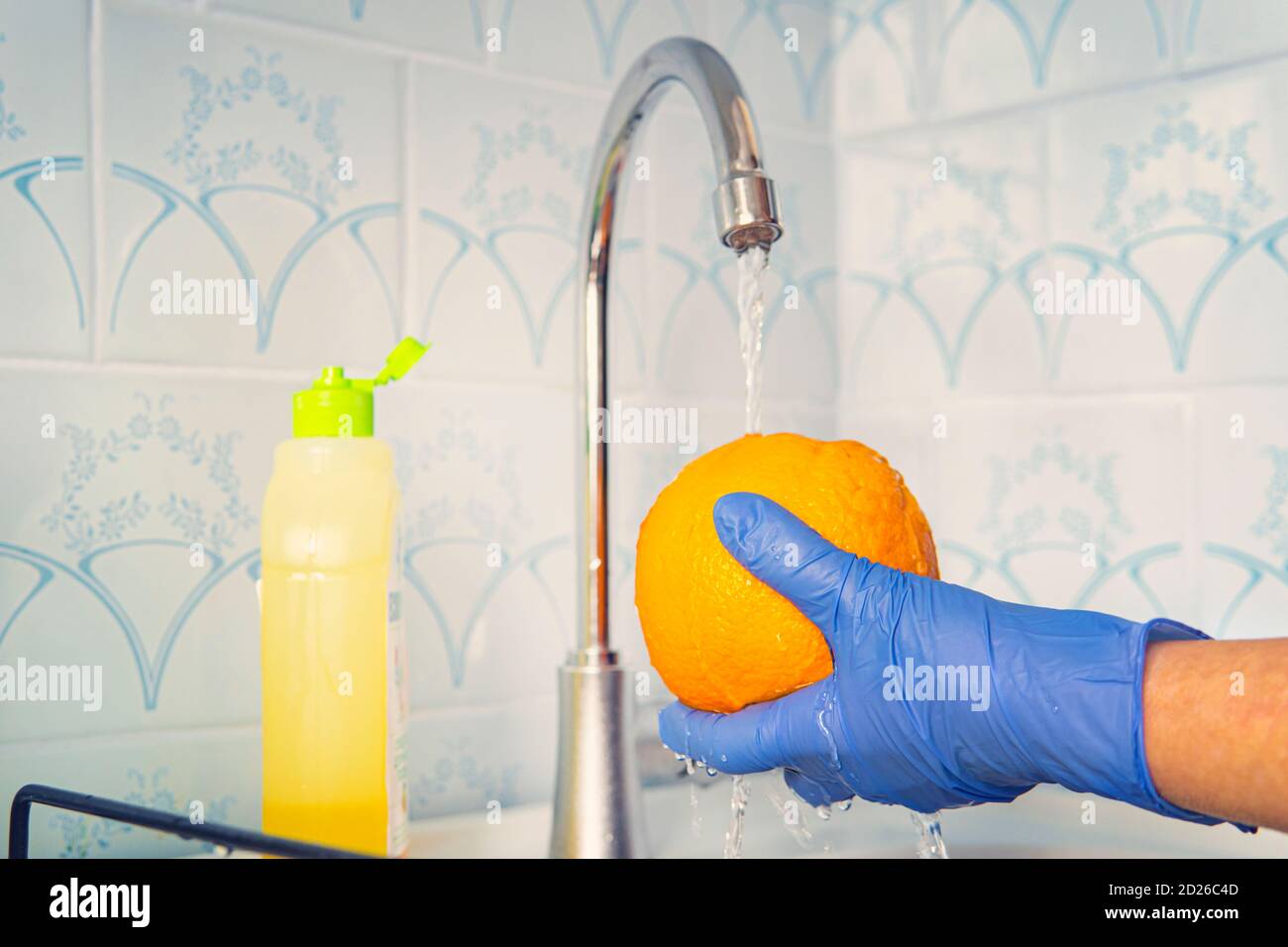 La persona lava la frutta con sapone ecologico per il lavaggio in una cucina con pareti blu. Decontaminazione e disinfezione dei prodotti dal punto vendita. Prevenzione di Foto Stock