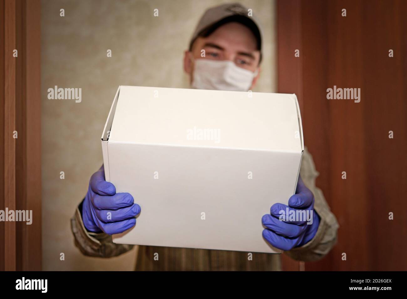 Concetto di merce consegnata durante la quarantena 2019-ncov. Il giovane uomo in maschera medica e guanti blu tiene in mano una scatola di cartone. Erogazione senza contatto Foto Stock