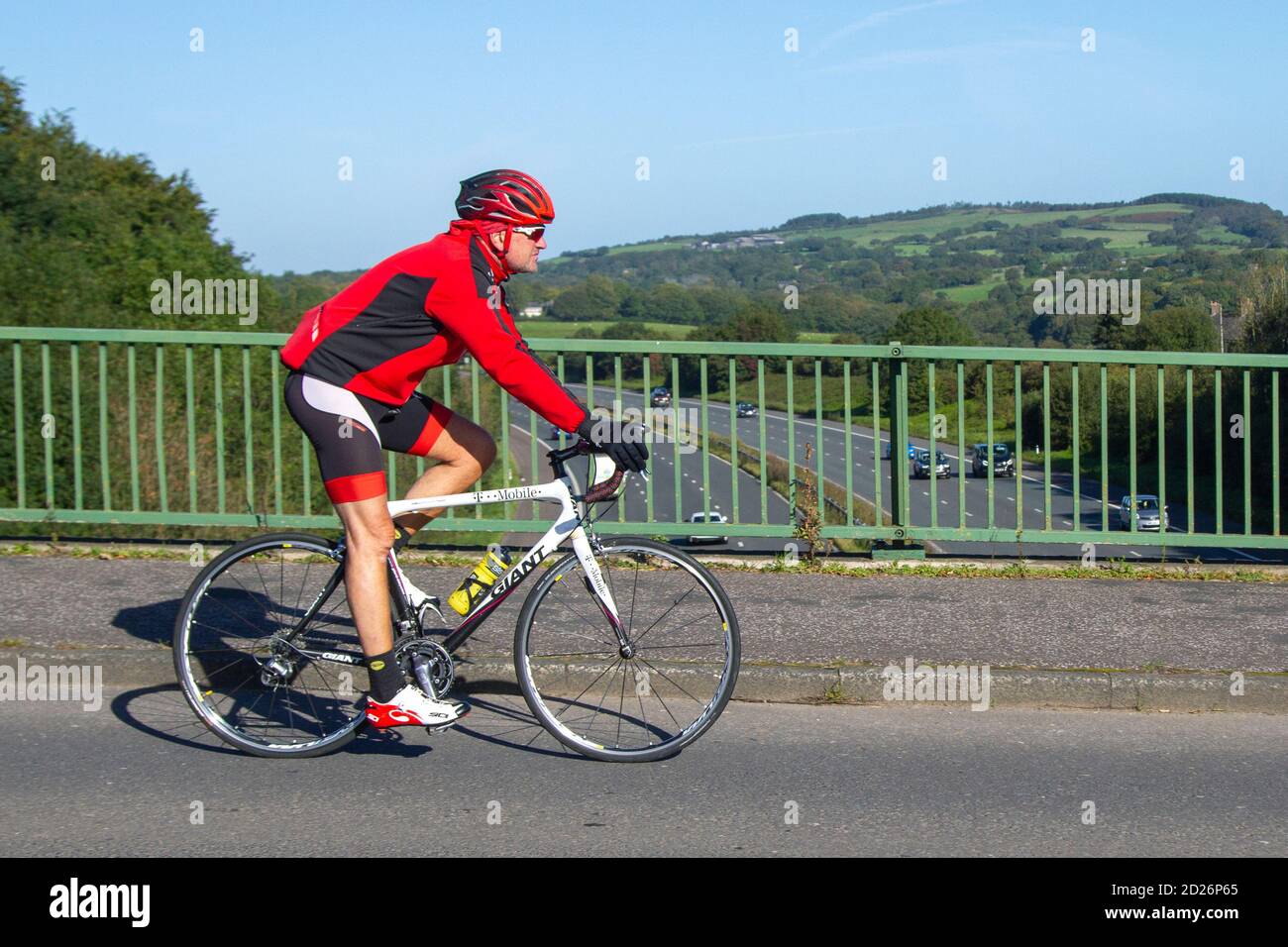 Ciclista maschile equitazione GIGANTE (T-Mobile) sport bianco bici da strada sulla strada di campagna che attraversa il ponte autostradale nella rurale Lancashire, Regno Unito Foto Stock