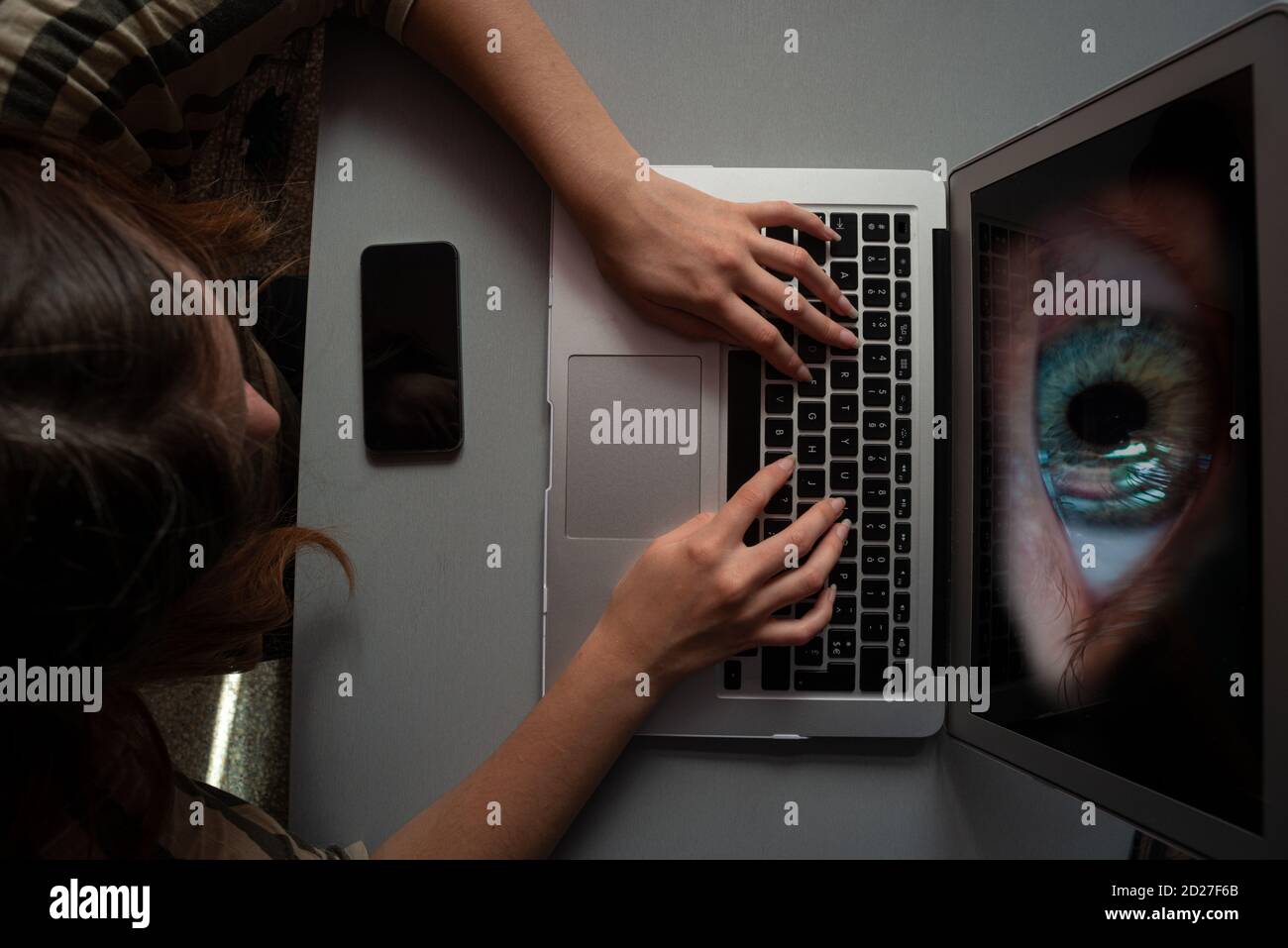 giovane donna che utilizza il computer per lo shopping o il lavoro infettato con spyware o malwear, grande occhio che guarda dallo schermo, concetto Foto Stock