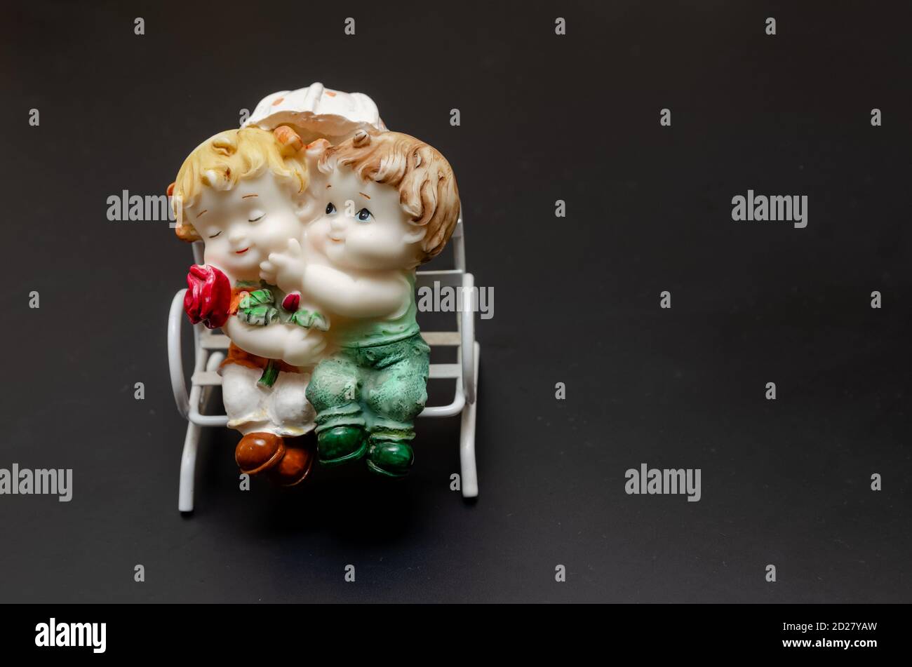 Figurine in ceramica di bambini su una panchina su un nero sfondo Foto Stock