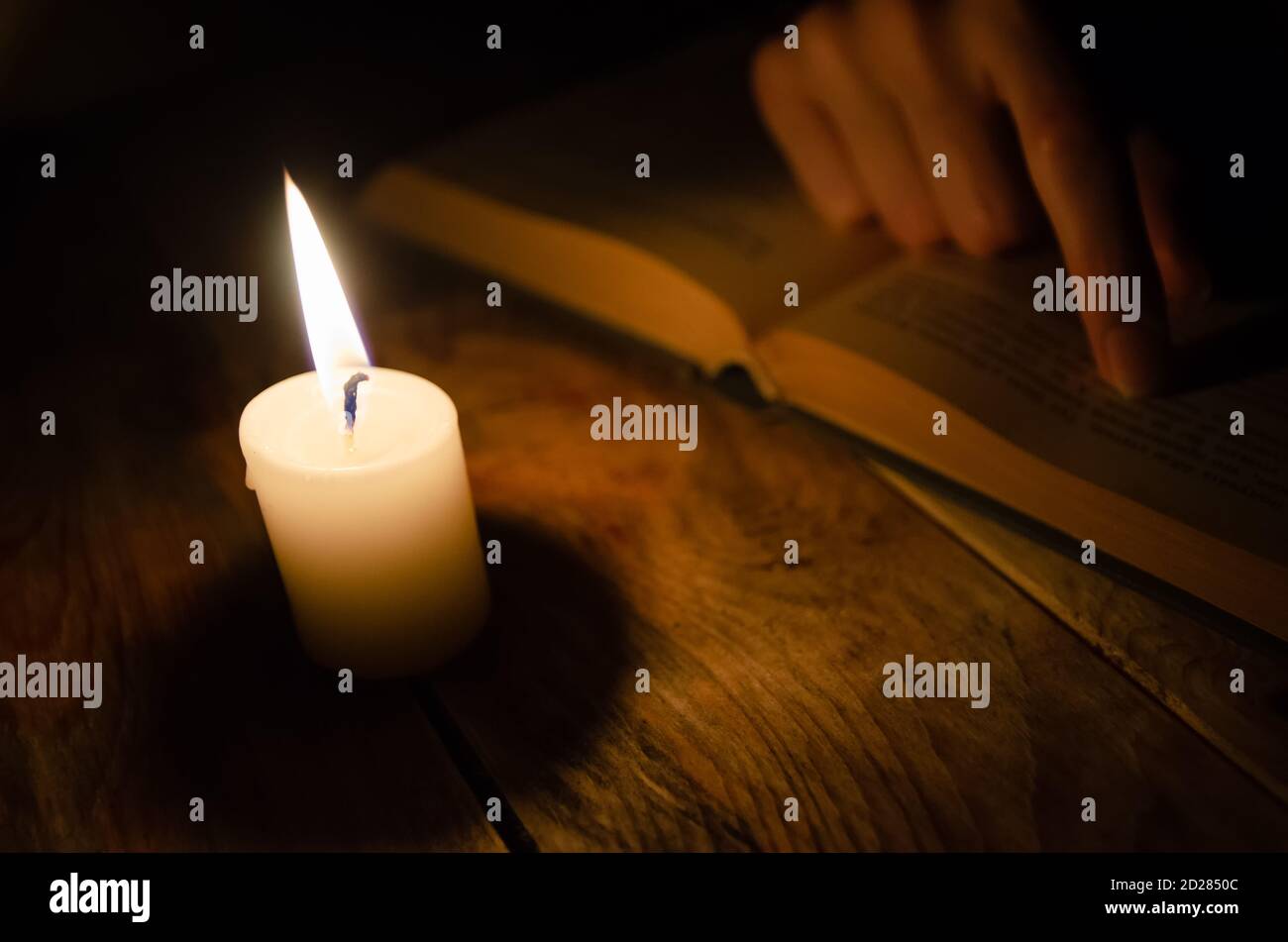 apri il libro, un dito su un libro e una candela che brucia su un tavolo di legno al buio Foto Stock