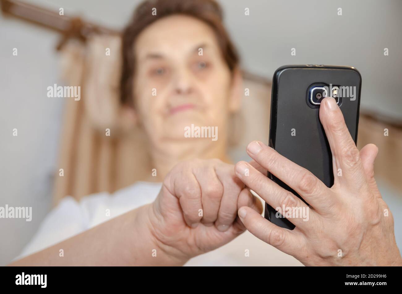 la donna anziana con i capelli scuri tiene un telefono cellulare nero davanti a lei, lo guarda e tocca il dito sullo schermo Foto Stock