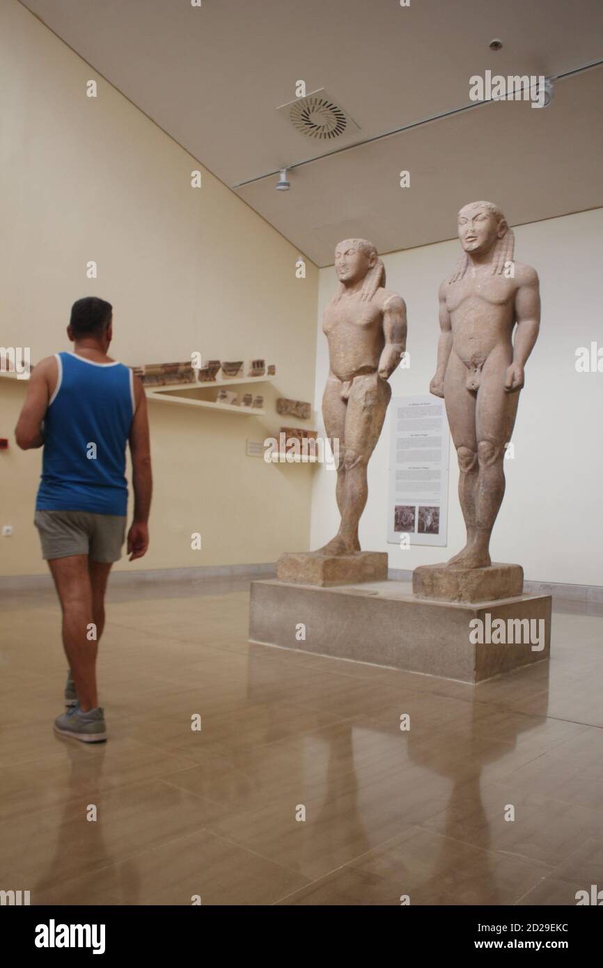 Un uomo che cammina tra Cleobis e Biton, i giganti Kouroi di Delfi nel museo archeologico del sito in Grecia Foto Stock