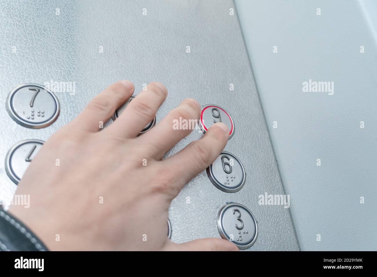 La mano dell'uomo ha premuto il pulsante dell'ascensore con il numero 9, Braille Foto Stock