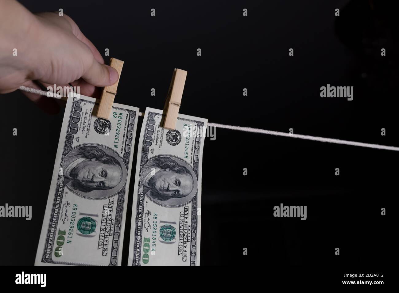 la mano dell'uomo appende i dollari su uno sfondo nero usando i clothespins su un concetto di corda. di soldi sporchi. Foto Stock