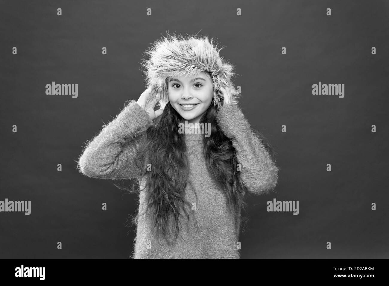 Tenere la testa in calore. Sensazione di caldo. Bambino lunghi capelli morbidi hat. In inverno il concetto di moda. Cappello caldo per il freddo inverno. Kid ragazza sfondo rosso. Soffice pelliccia accessorio. Stagione invernale. Il concetto di shopping. Foto Stock