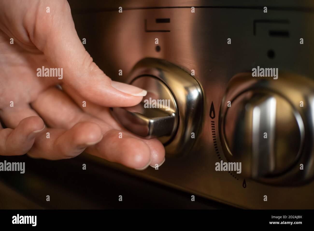 la mano della donna accende un interruttore su un acciaio inossidabile stufa a gas primo piano Foto Stock