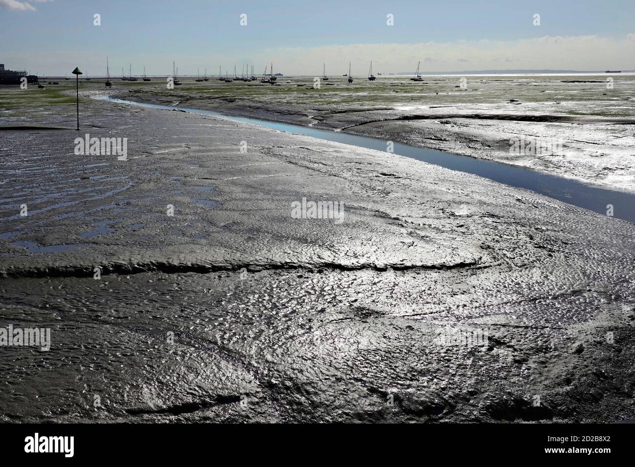 Il sole scintilla sulle distese di fango sull'estuario costiero del Tamigi al largo di Leigh sui canali di drenaggio del mare Southend Pier naviga in Essex Inghilterra Regno Unito Foto Stock