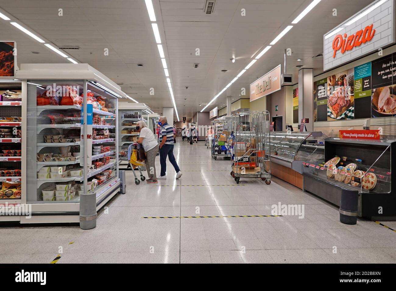 Sainsburys supermercato corsia di shopping e scaffali di cibo coppia di acquirenti Carrello di spinta che indossa pandemic coronavirus covid 19 maschere viso Inghilterra REGNO UNITO Foto Stock