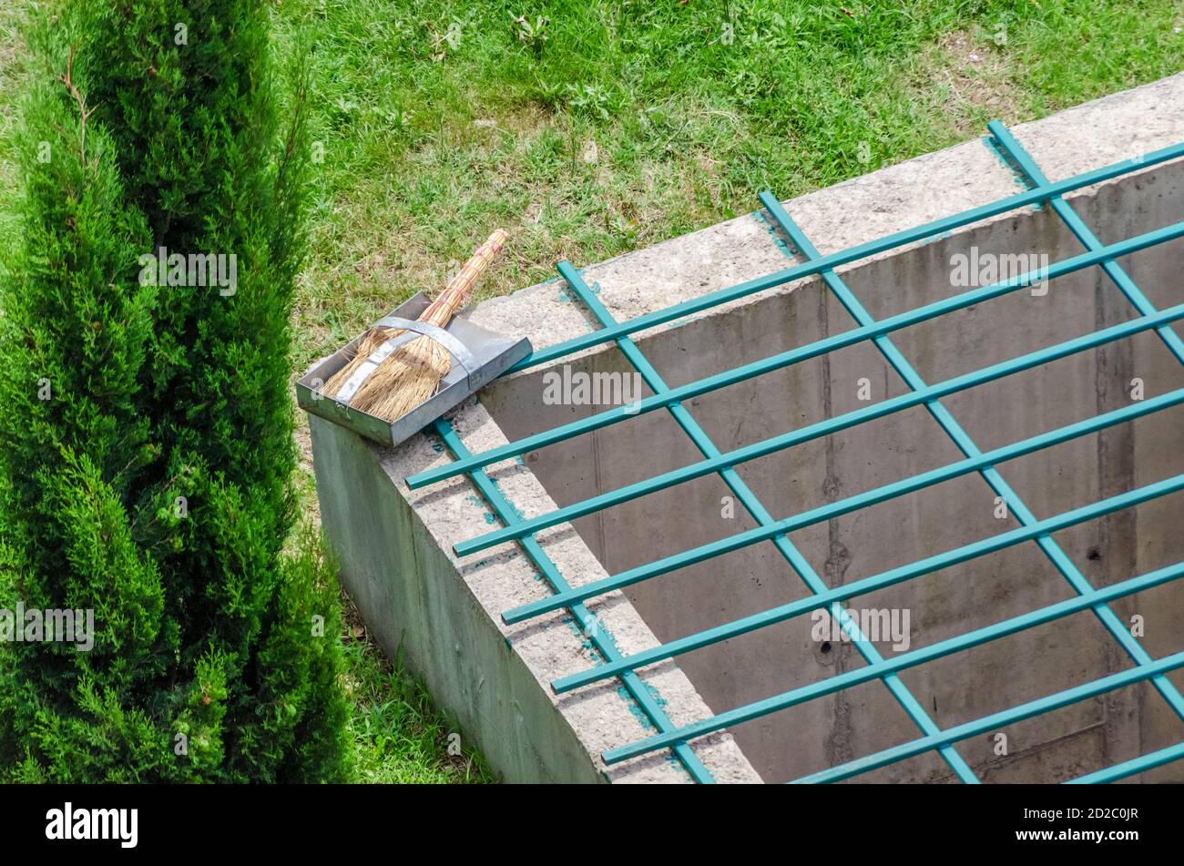 Pulizia del parcheggio. Scopa con casseruola sdraiata su struttura metallica sullo sfondo di erba verde. Vista dall'alto della foto Foto Stock