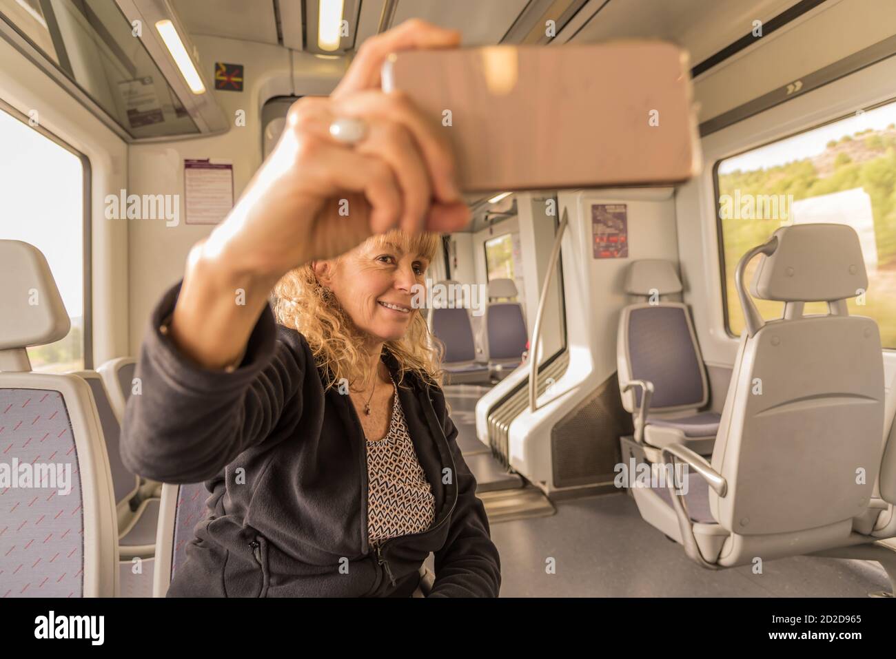 Una donna adulta che prende un selfie sul treno solitario con il suo telefono Foto Stock