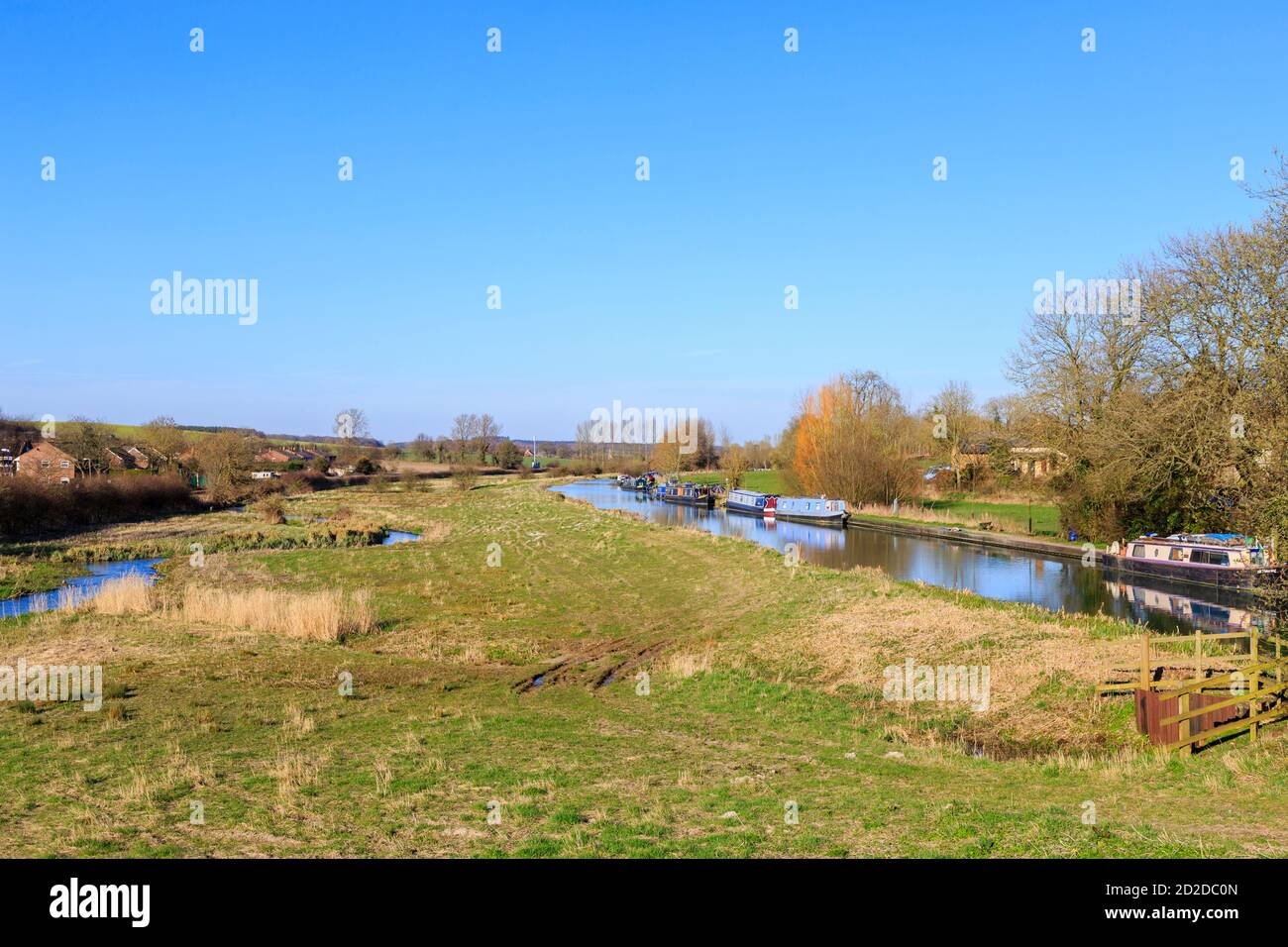 Vista a est delle barche strette ormeggiate sul ramo Bruce del Kennett e sul canale Avon a Great Bedwyn, Wiltshire, Regno Unito con Bedwyn Brook (River Dun) Foto Stock