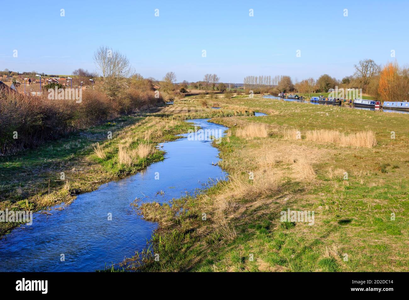 Vista a est delle barche strette ormeggiate sul ramo Bruce del Kennett e sul canale Avon a Great Bedwyn, Wiltshire, Regno Unito con Bedwyn Brook (River Dun) Foto Stock