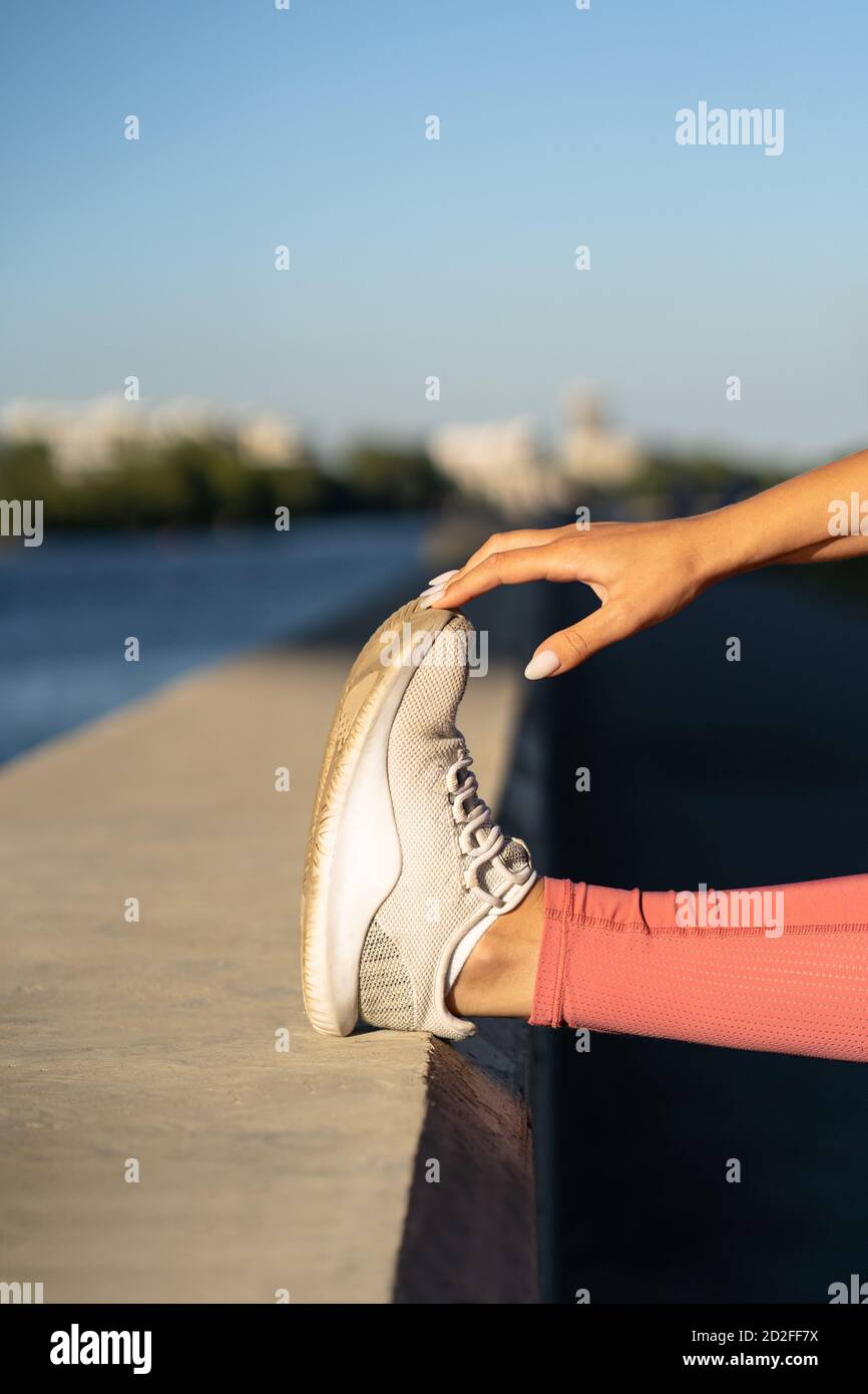 Primo piano di muscoli stretching femminile facendo allenamento funzionale, facendo esercizi per le gambe prima di un allenamento. Fitness, corsa urbana. Foto Stock