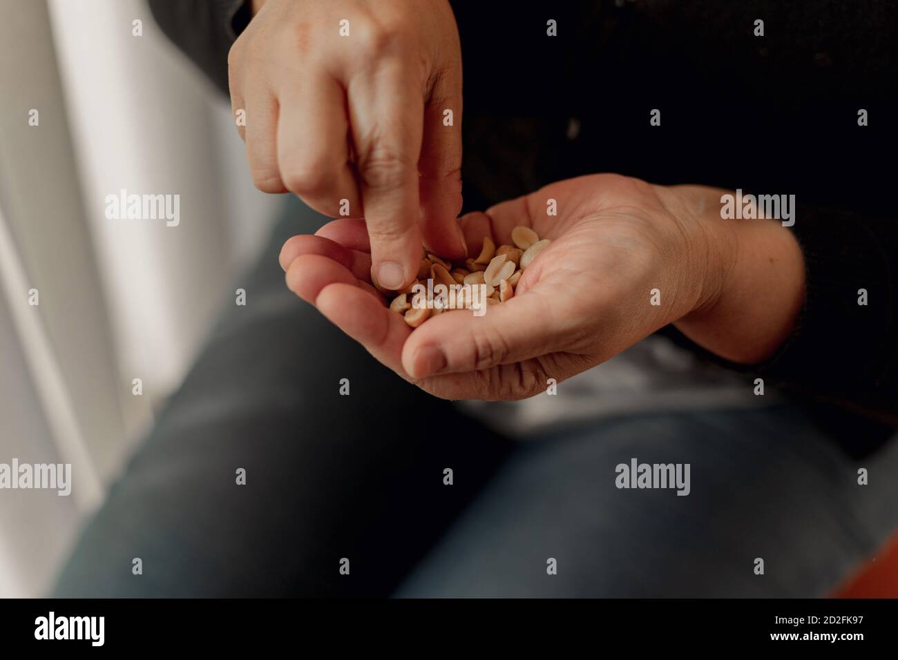 Dettaglio delle mani di una donna adulta che tiene un mazzo di arachidi e prenderle con la mano destra Foto Stock