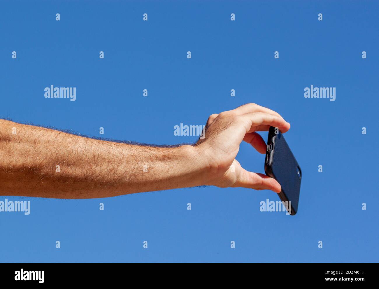 Una foto astratta che mostra l'avambraccio e la mano di un giovane adulto caucasico mentre sta tenendo uno smartphone per prendere un selfie. Si tratta di un concetto semplice ima Foto Stock