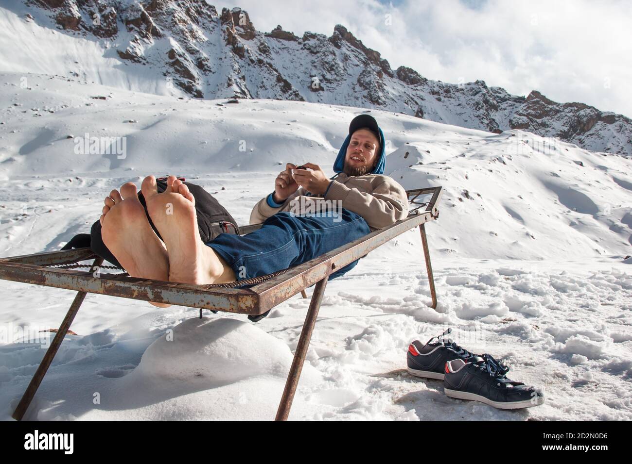 Un uomo in inverno con piedi nudi riposa su un letto di ferro in montagna. Concetto di divertimento per le vacanze invernali Foto Stock