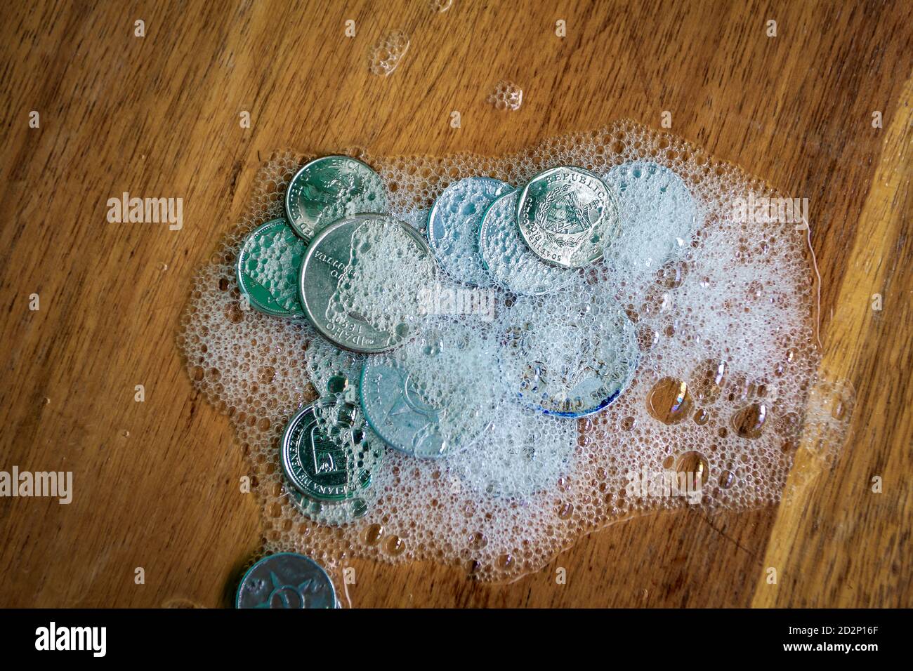 Gruppo di monete ricoperte di schiuma su una superficie di legno Foto Stock