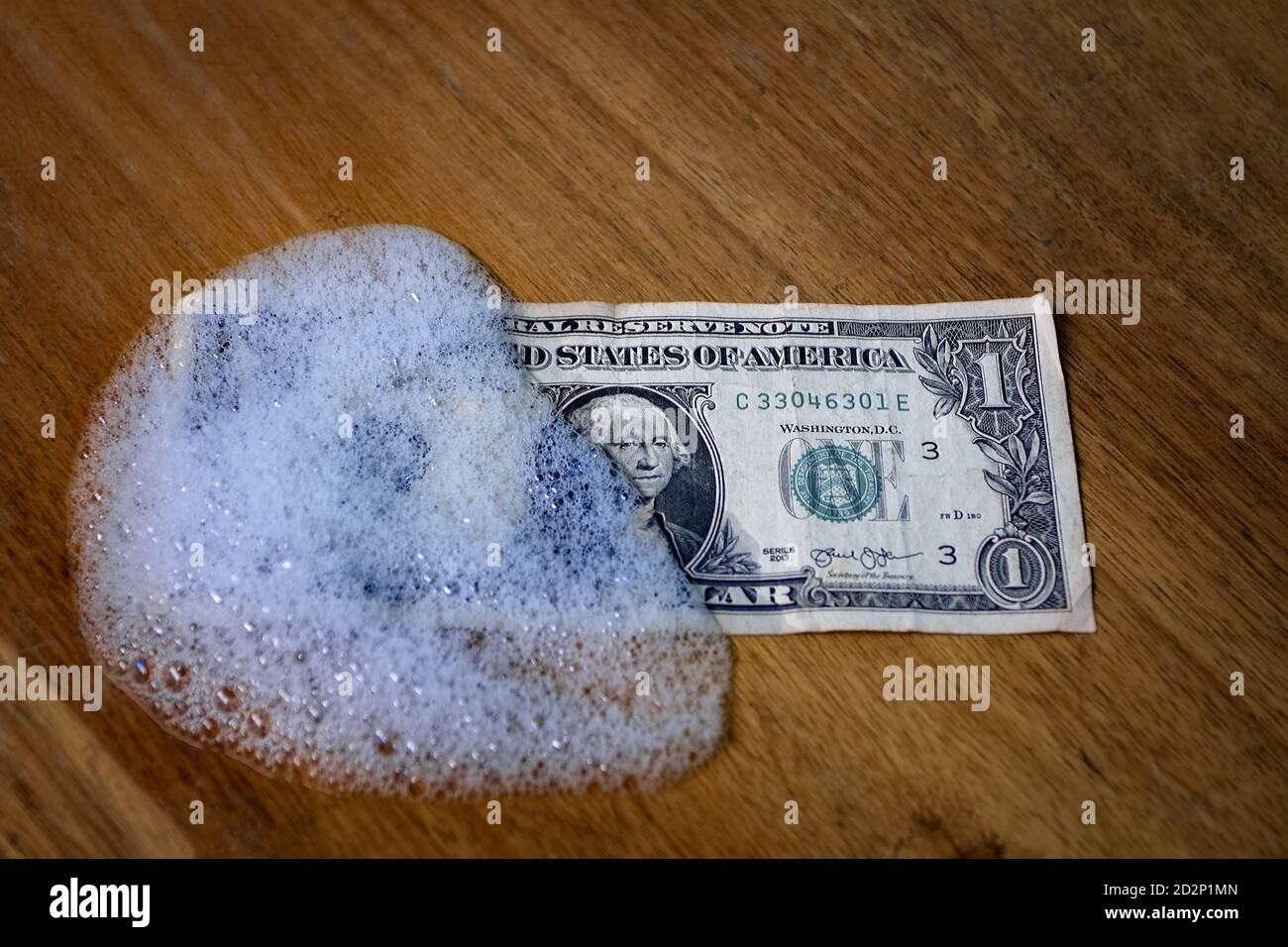 Una fattura di un dollaro parzialmente coperta da schiuma su un superficie in legno Foto Stock