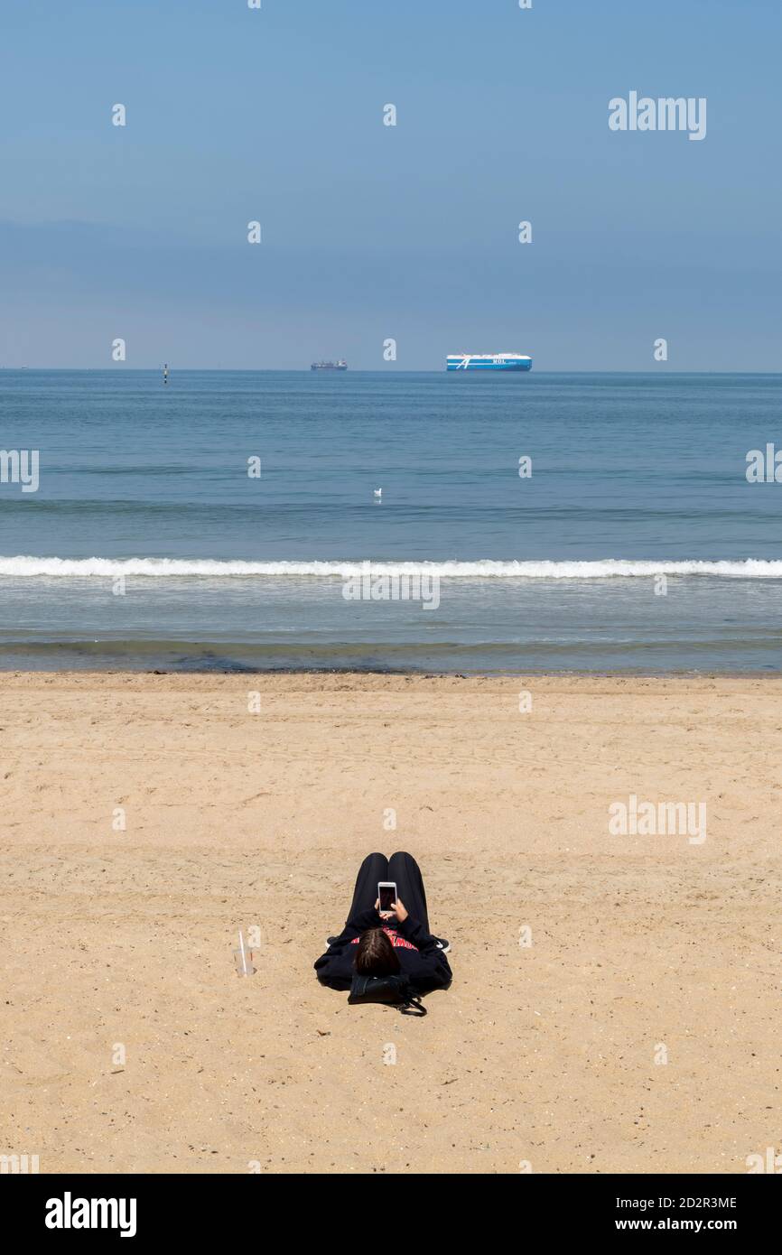 Giovane donna si trova sulla spiaggia mentre usa il suo smartphone. Foto Stock