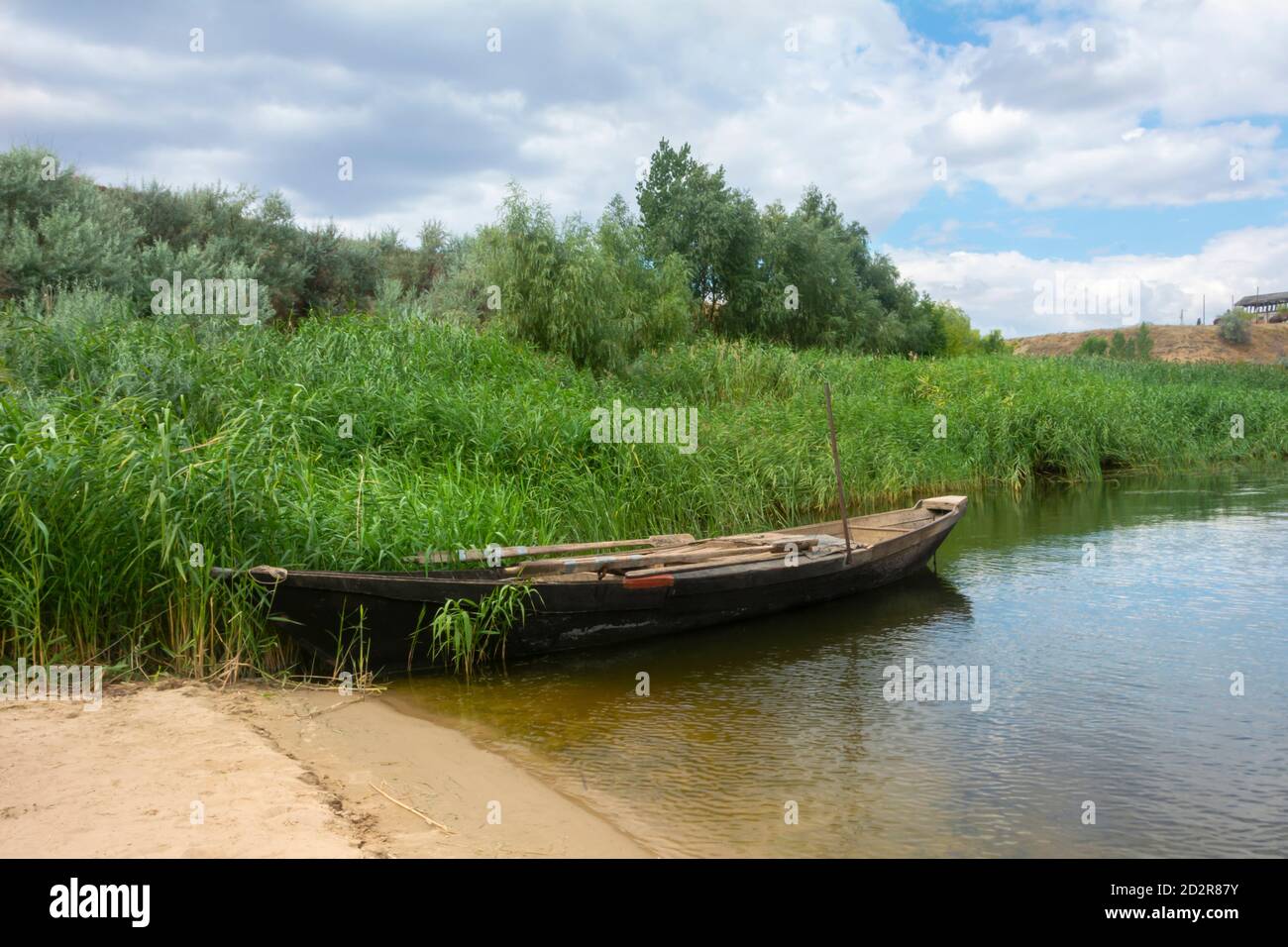 Vecchia barca di pescatori di legno sul fiume. Splendido paesaggio estivo con alte canne sulla riva, lago e cielo con nuvole. Nave retrò sull'acqua. Foto Stock