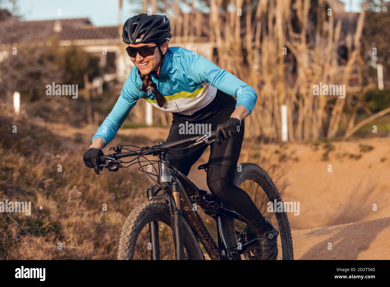 Sportswoman in caschetto nero e abbigliamento sportivo blu con occhiali in mountain bike su pista di allenamento Foto Stock