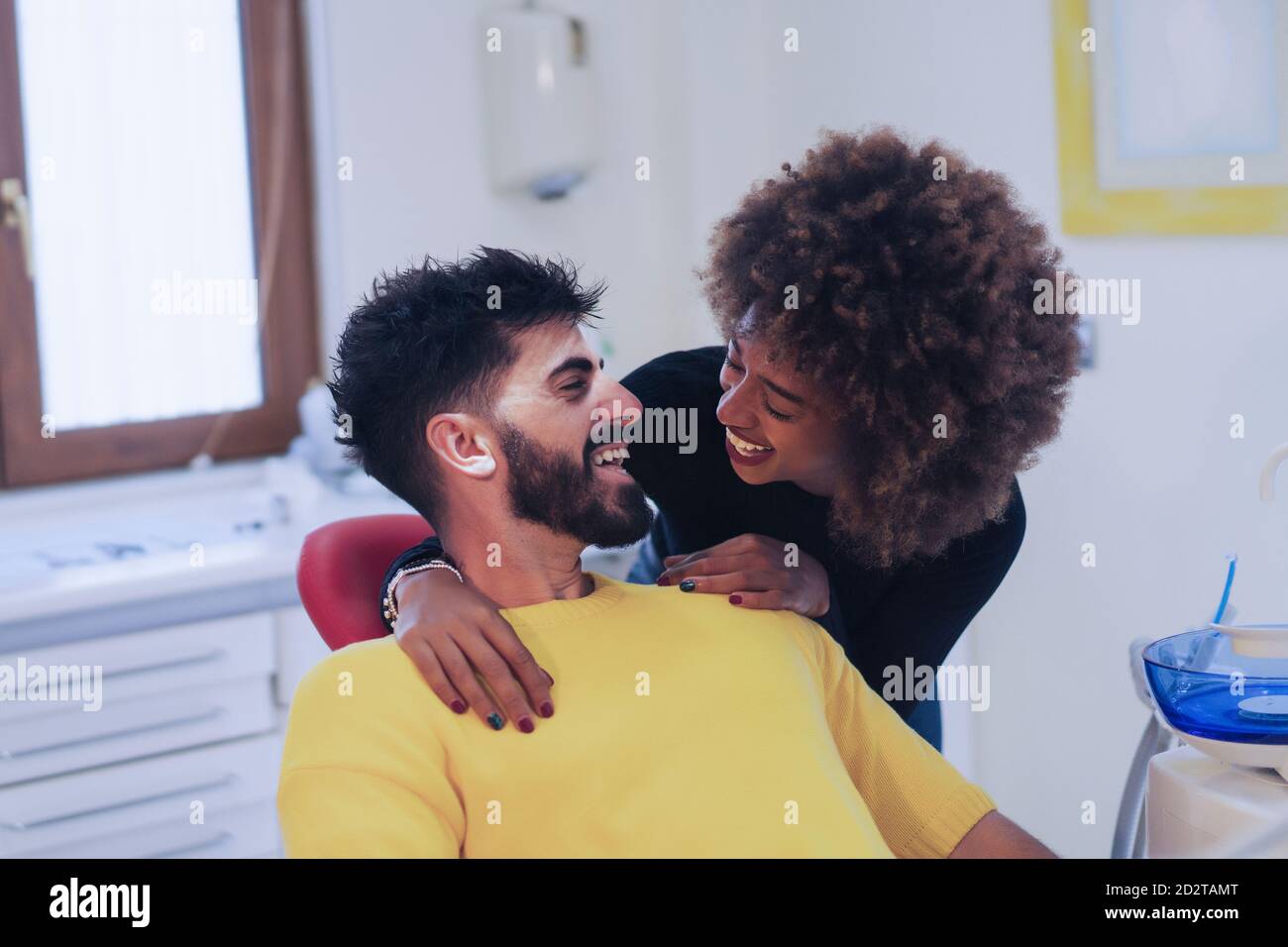 Giovane donna afroamericana sorridente e guardando alato ispanico uomo mentre visita dentista insieme Foto Stock