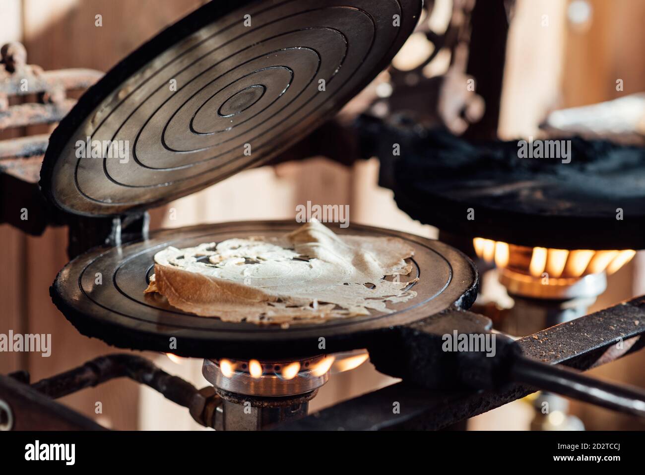 Closeup processo di preparazione di biscotti tradizionali catalani di neula in ferro da stiro a base di waffle su fornelli a gas Foto Stock