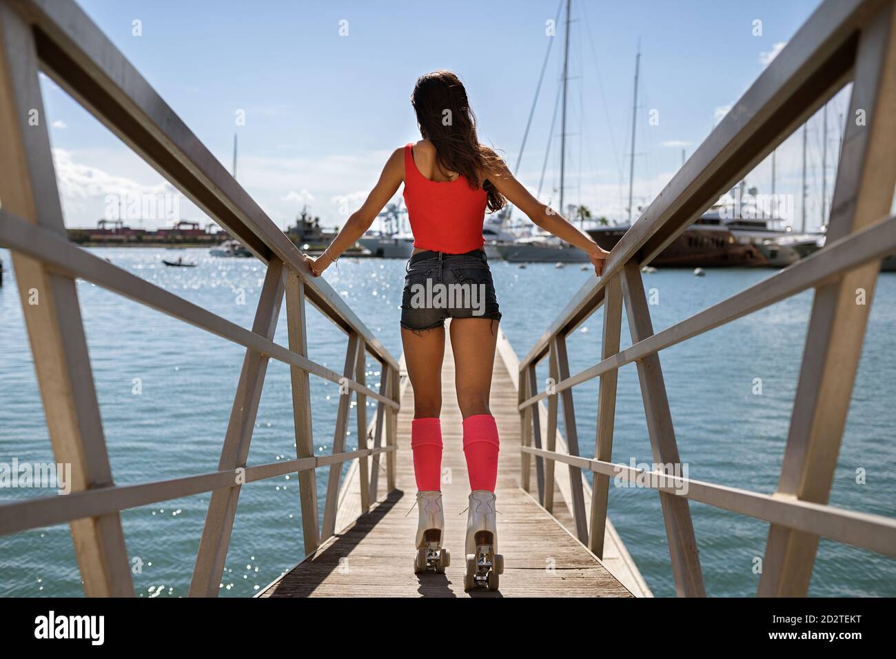 Vista posteriore di un'irriconoscibile pattinata a rulli femminile snella lungo il legno quay in città in estate Foto Stock