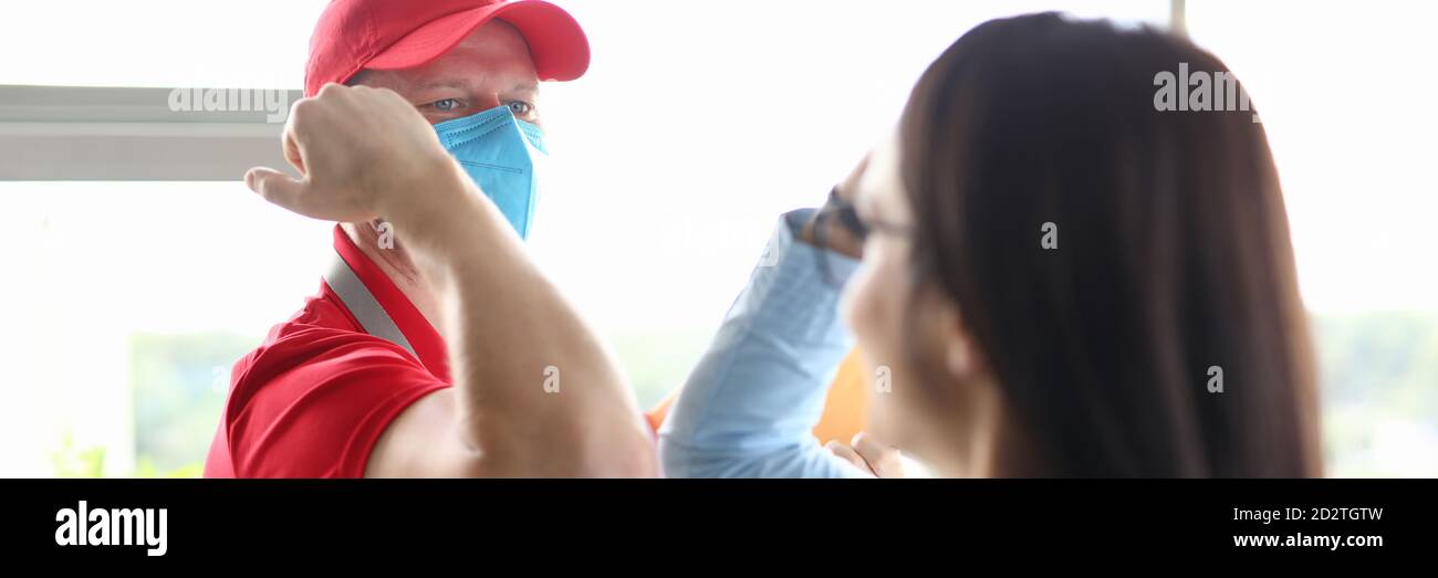 Il corriere che indossa una maschera medica protettiva saluta il cliente in modo sicuro. Foto Stock
