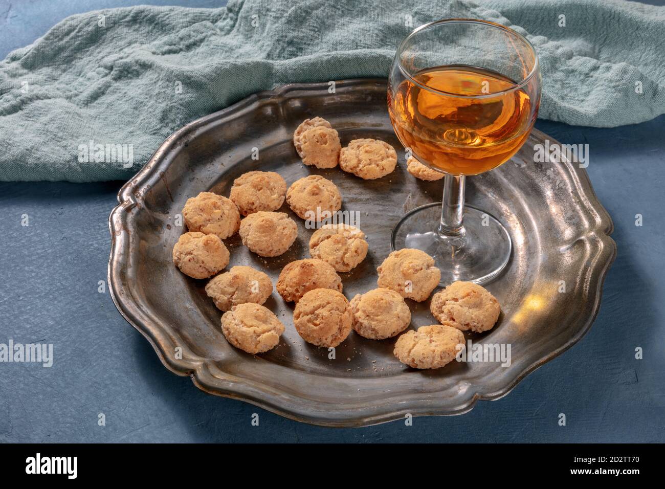 Amaretti, biscotti tradizionali italiani alle mandorle, con un bicchiere di liquore amaretto, su fondo blu scuro Foto Stock