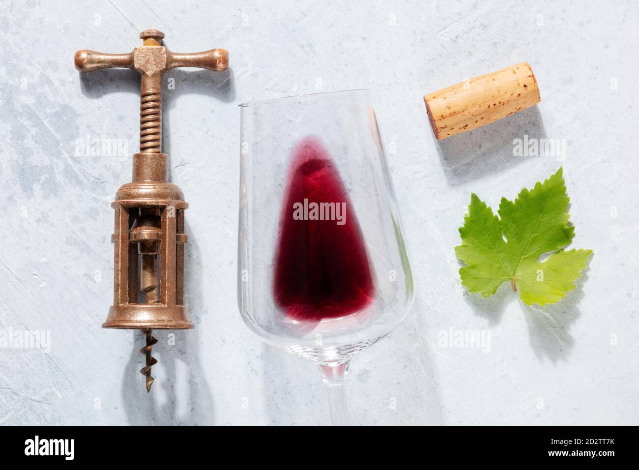 Vista dall'alto della composizione piatta del vino rosso con un'uva, un cavatappi d'annata, un tappo di vino e una foglia di vite, ripresa dall'alto su uno sfondo chiaro Foto Stock