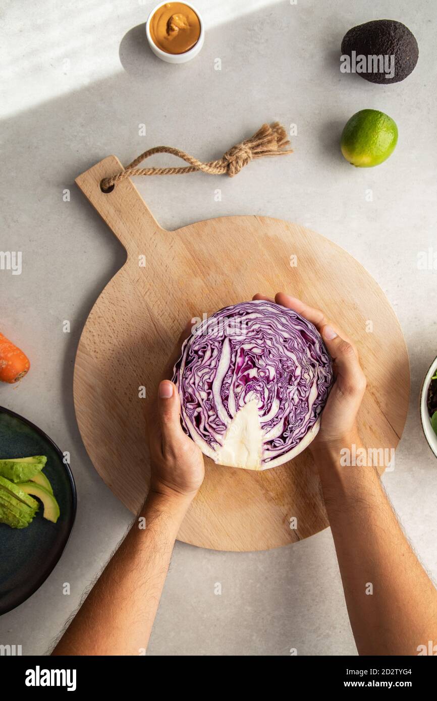 Vista dall'alto della persona anonima del raccolto che mette a metà il rosso fresco cavolo su tagliere di legno mentre preparano l'insalata deliziosa dentro cucina Foto Stock
