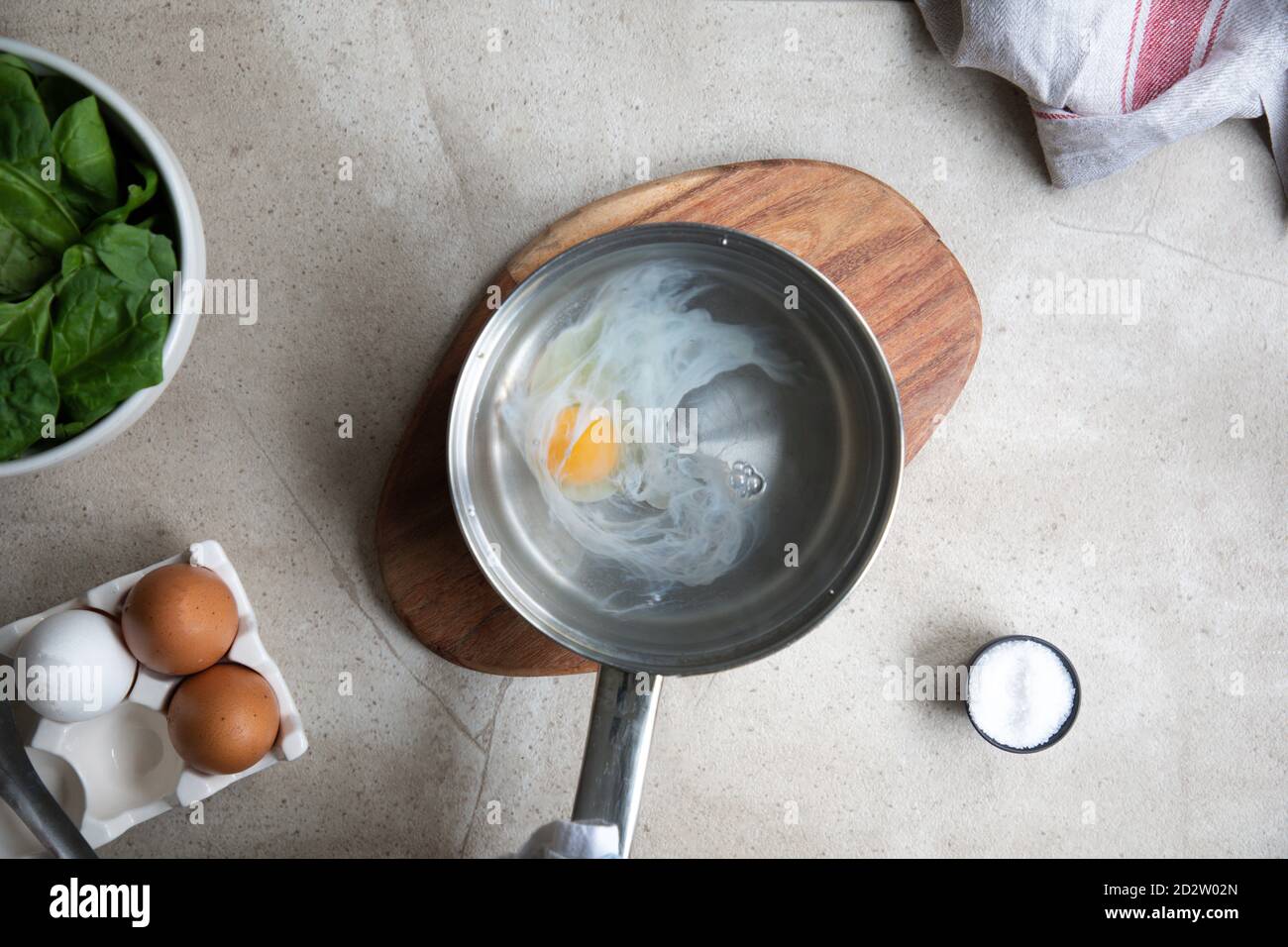 Vista dall'alto della pentola in metallo con acqua bollente e uova durante la preparazione delle uova in camicia su un tavolo da cucina con ingredienti Foto Stock