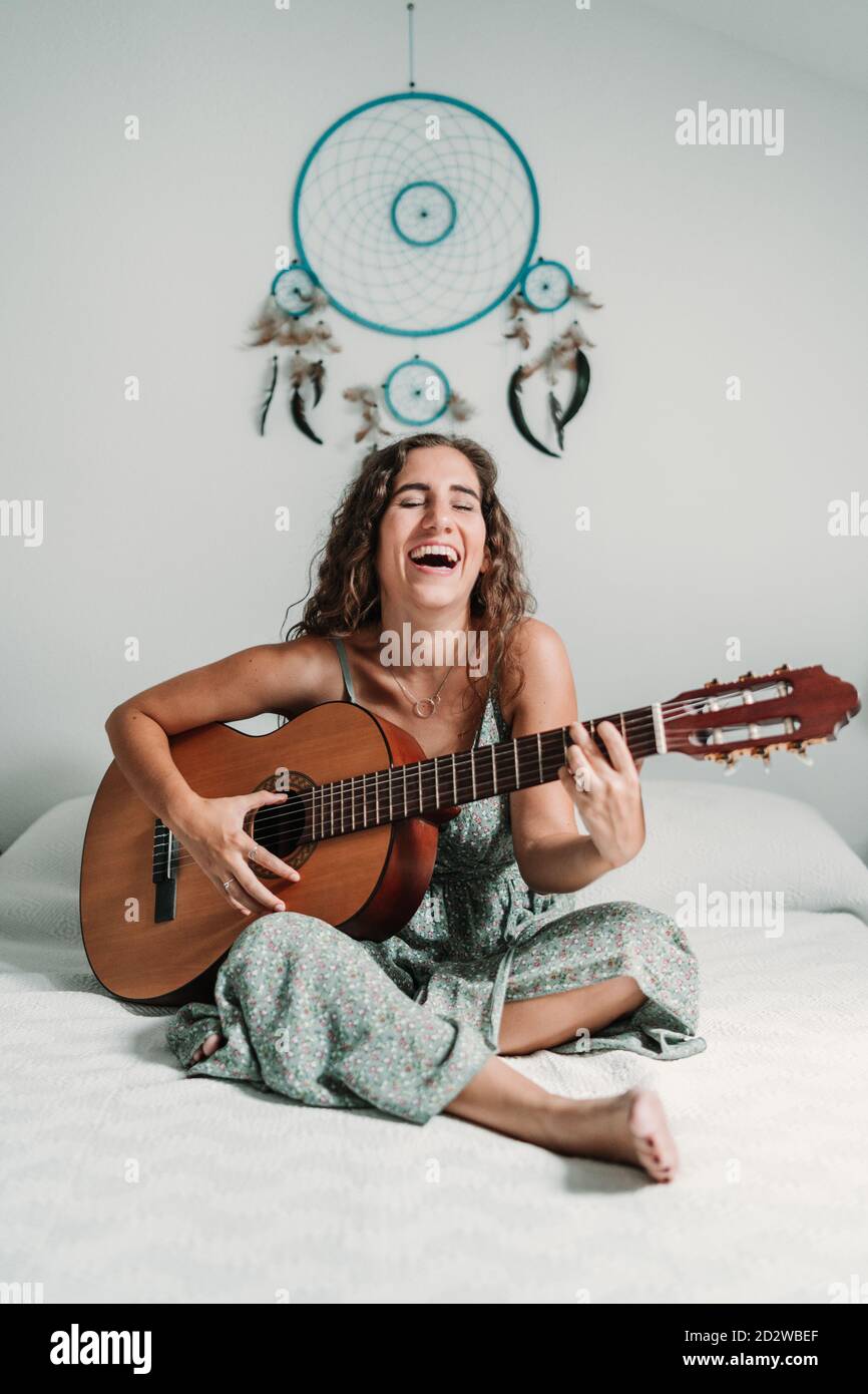 Allegra chitarrista etnica seduta su un comodo letto a casa e suonare  strumento musicale acustico a occhi chiusi Foto stock - Alamy