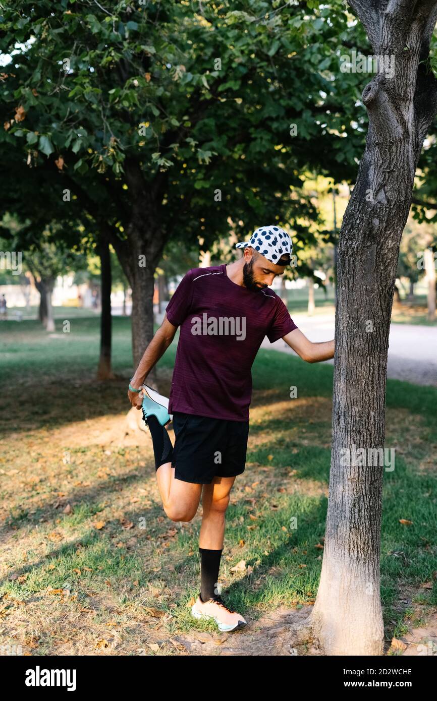 Concentrato atleta maschile in sportswear gambe allungare mentre si riscalda durante l'allenamento nel parco Foto Stock