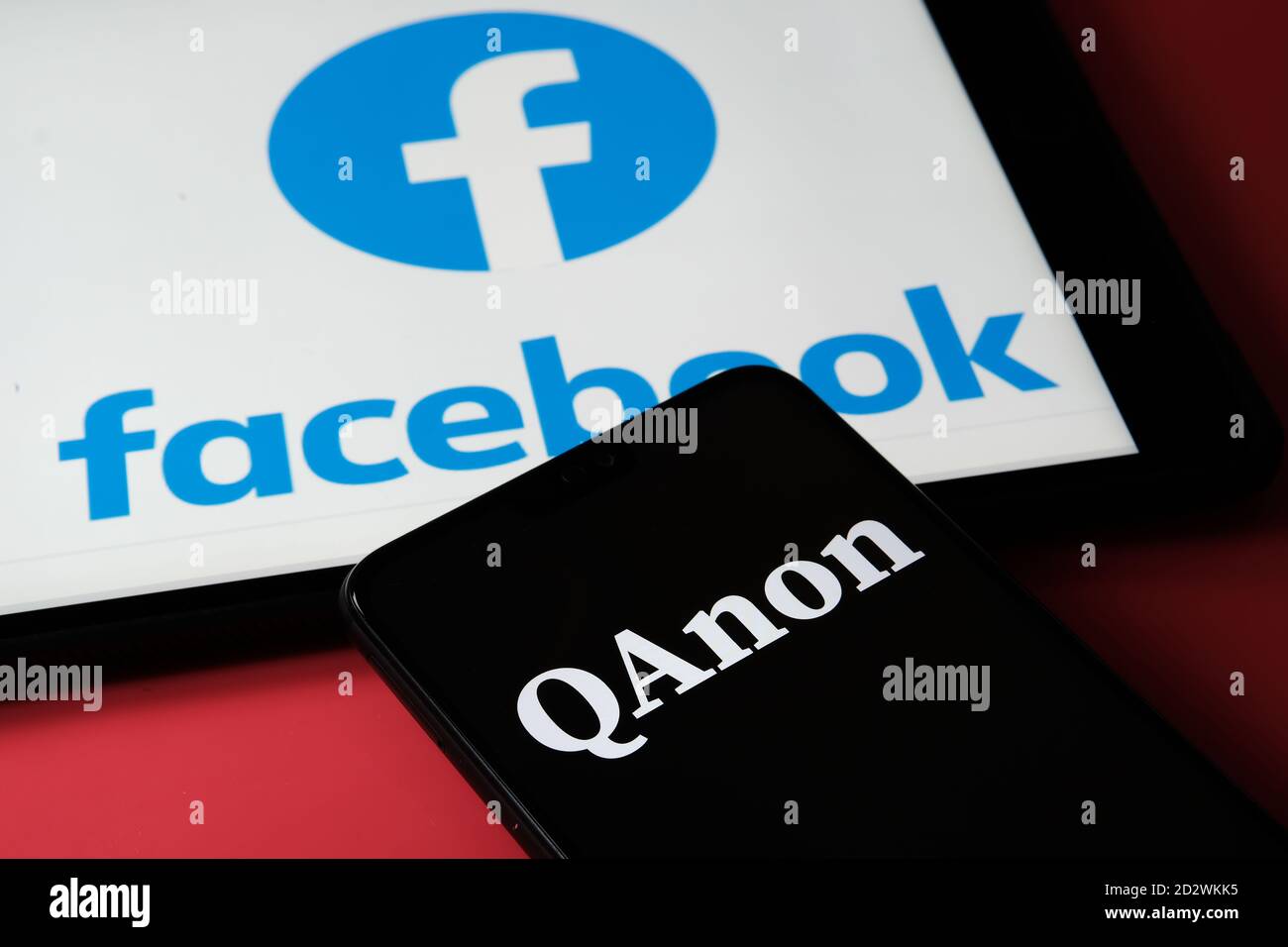 QAnon vs FACEBOOK. Logo aziendale QAnon visualizzato sullo smartphone, posizionato sul tablet con il logo Facebook. Concetto di divieto di QAnon su soc Foto Stock