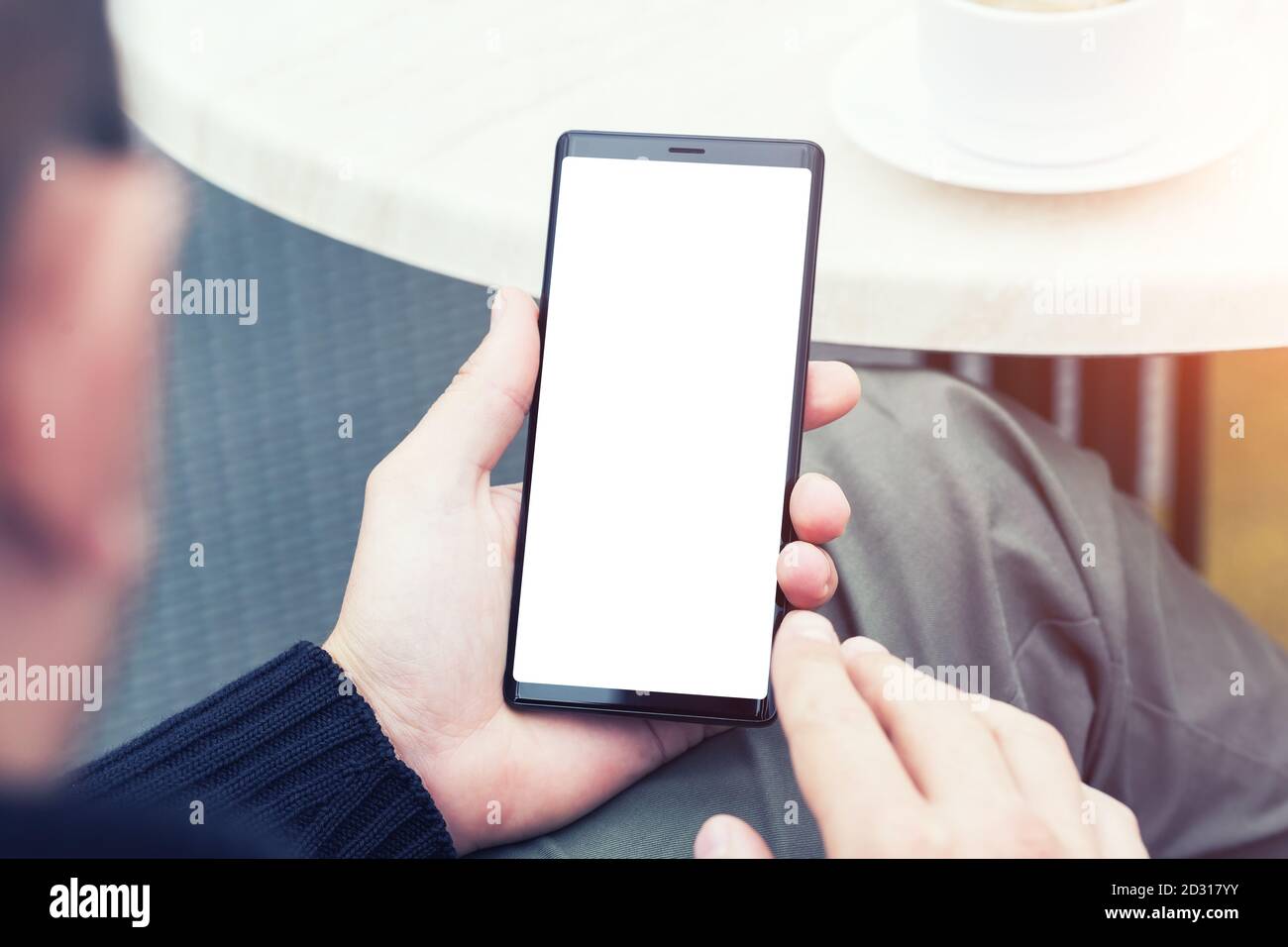 Primo piano dello smartphone portatile con le mani dell'uomo e schermata vuota dello spazio di copia. Immagine di un uomo seduto a un tavolo con un caffè in caffetteria e utilizzando mobil Foto Stock