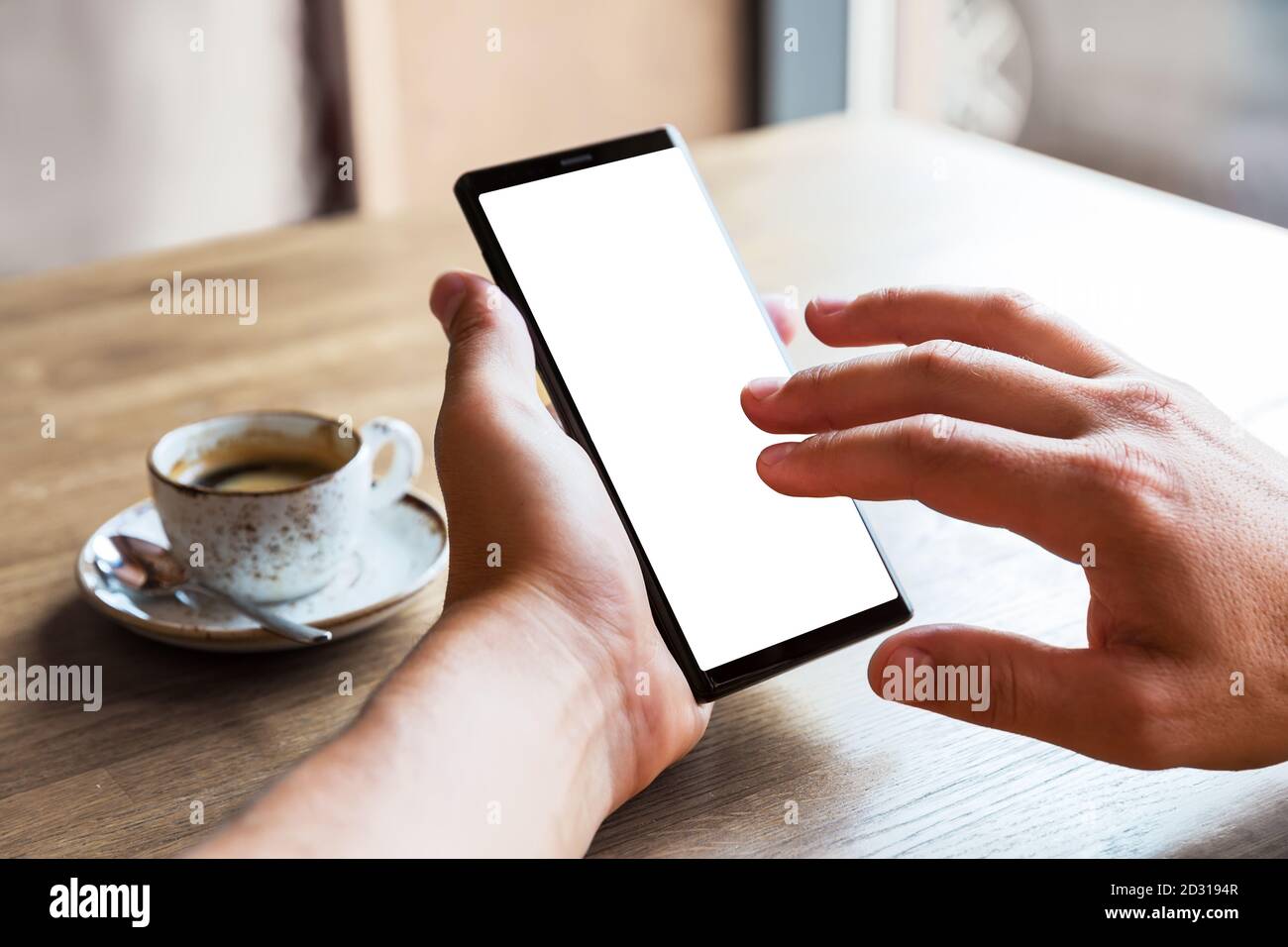 Primo piano dello smartphone portatile con le mani dell'uomo e schermata vuota dello spazio di copia. Immagine di un uomo seduto a un tavolo con un caffè in caffetteria e utilizzando mobil Foto Stock