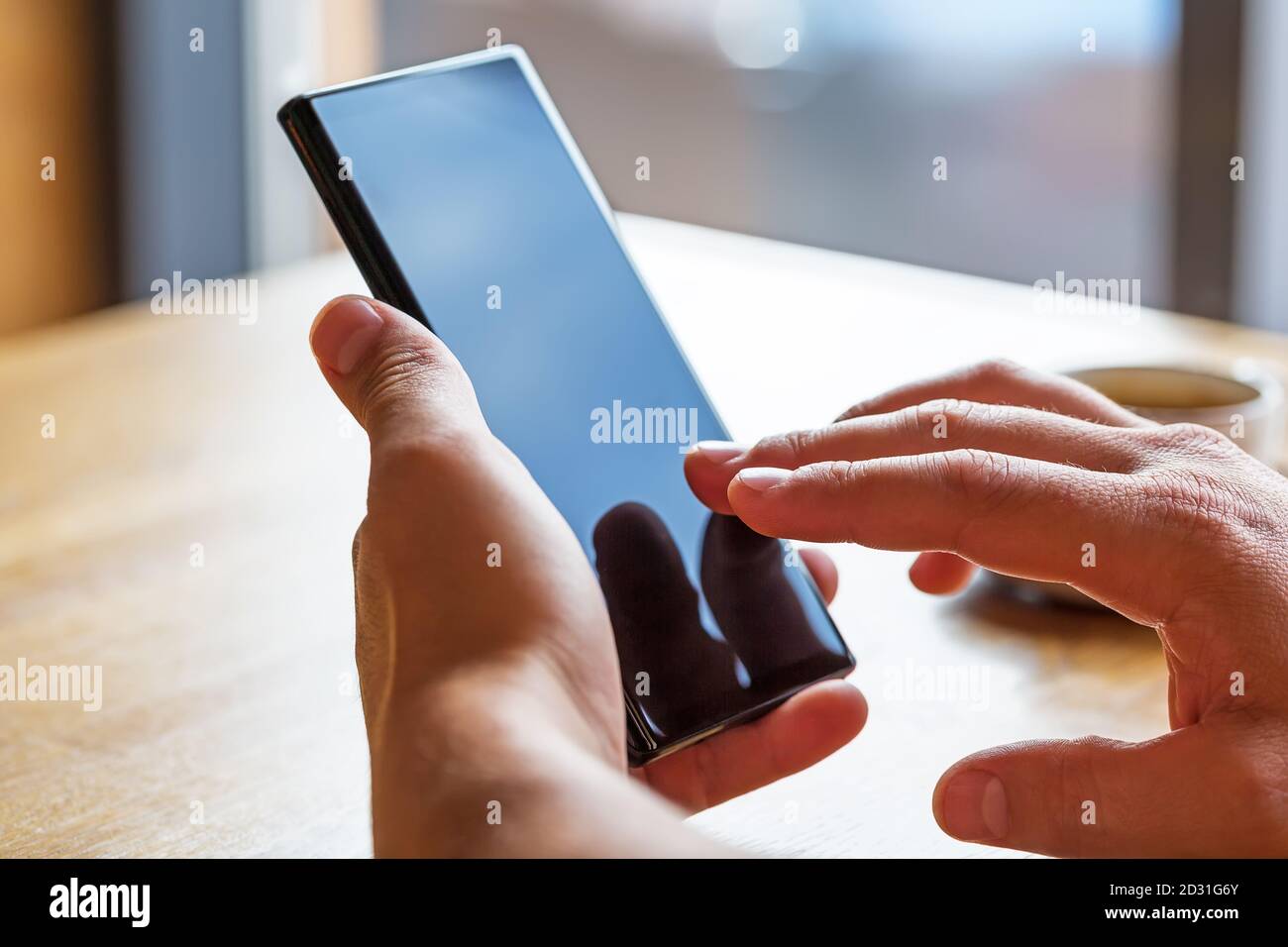 Primo piano dello smartphone portatile con le mani dell'uomo e schermata vuota dello spazio di copia. Immagine di un uomo seduto a un tavolo con un caffè in caffetteria e utilizzando mobil Foto Stock